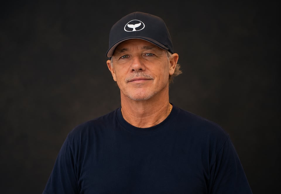 Portrait of the marine life artist Wyland wearing a whale-tail cap against a dark backdrop